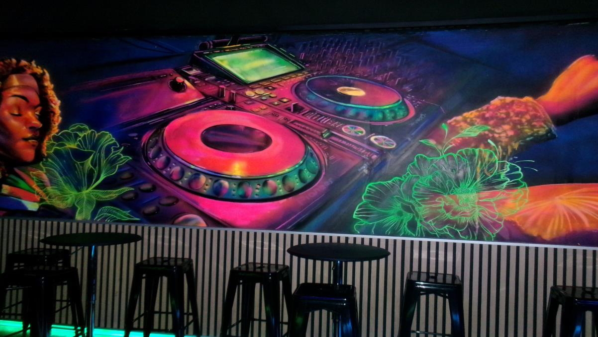 Interior de Karaoke Tanit con mural neón y cabina DJ